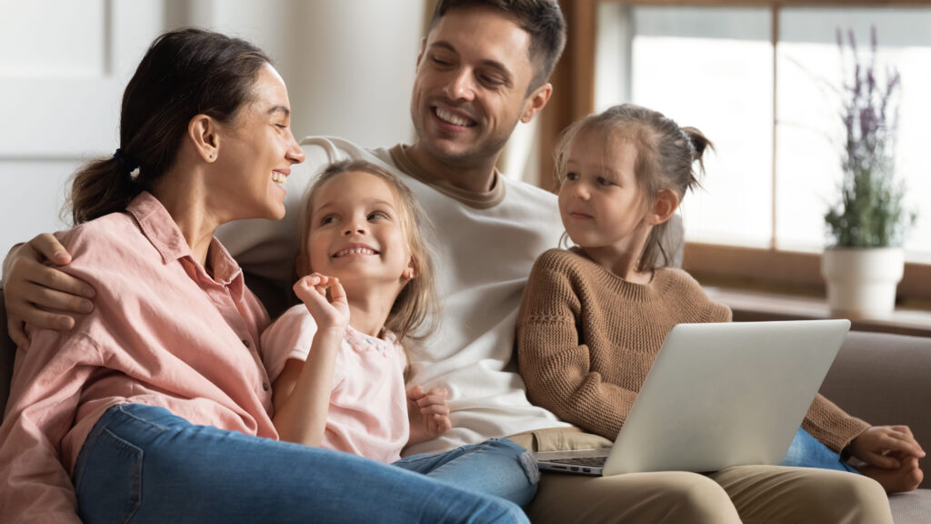 Familia de padre, madre y dos niñas pequeñas hablando y mirando el ordenador