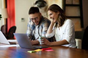 Una mujer y un hombre mirando la pantalla del ordenador y conriendo