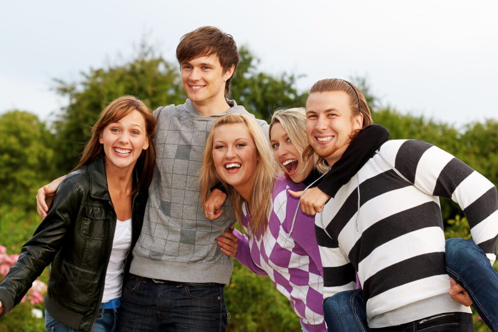 Cinco jóvenes abrazándose de lado y riéndose