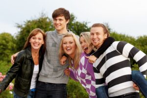 Cinco jóvenes abrazándose de lado y riéndose