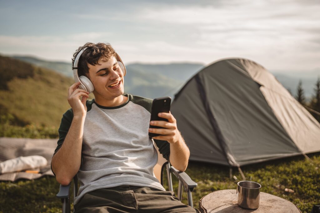 Chico joven en la montaña escuchando un podcast mientras mira el móvil.