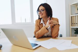Mujer en traje marrón y con gafas mientras lee lo que hay en la pantalla de su portátil