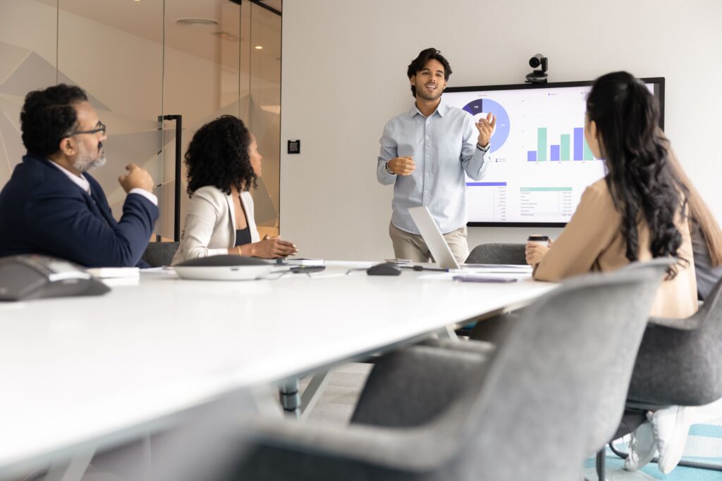 Hombre presentando en una pizara digital ante 2 muejres y 1 hombre