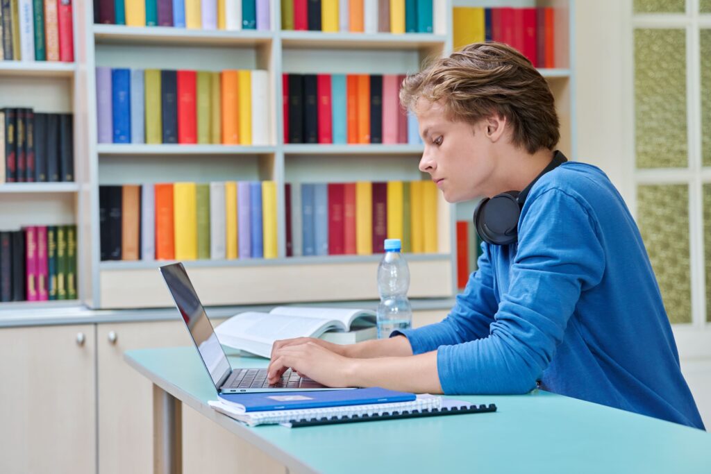 Un adolesctente mirando su portátil en la biblioteca