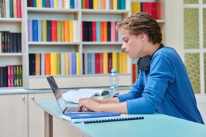 Un adolesctente mirando su portátil en la biblioteca